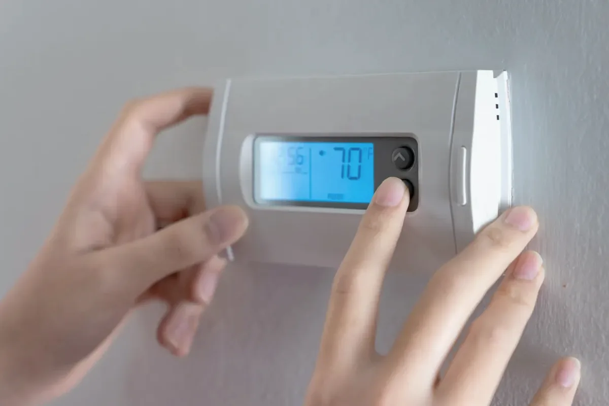 Hands adjusting a digital wall thermostat